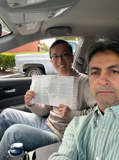 Javed and a student inside the car, holding passed DMV drive test paperwork