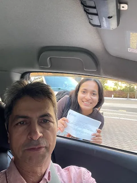 Javed and a student showing a passed DMV drive test slip through the car window