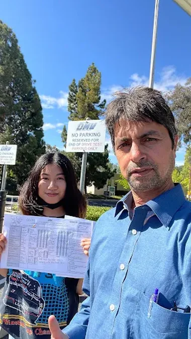 A student holding their passed California DMV drive test paperwork beside Javed, outside the Santa Clara DMV